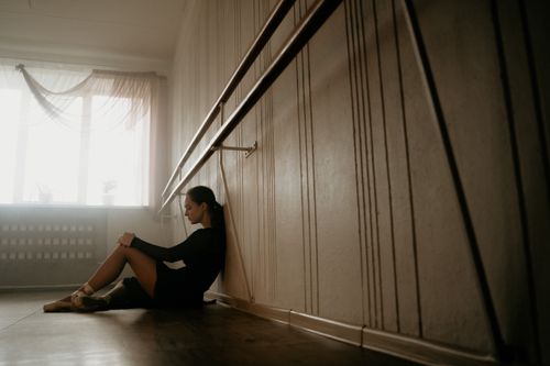 Free A young ballerina in a black leotard sits resting against a studio wall, lost in thought. Stock Photo