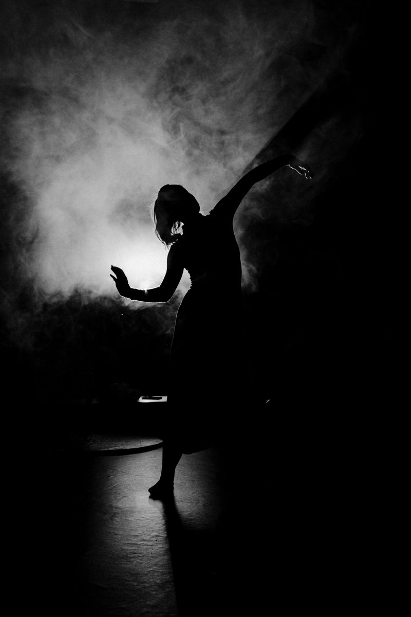 Black and white silhouette of a woman dancer performing on a smoky stage