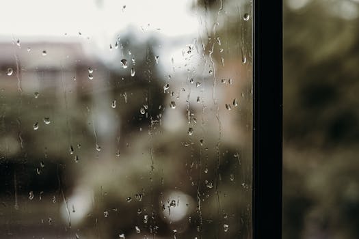 Close-up of raindrops on a window with a blurred view outside, creating a moody atmosphere.
