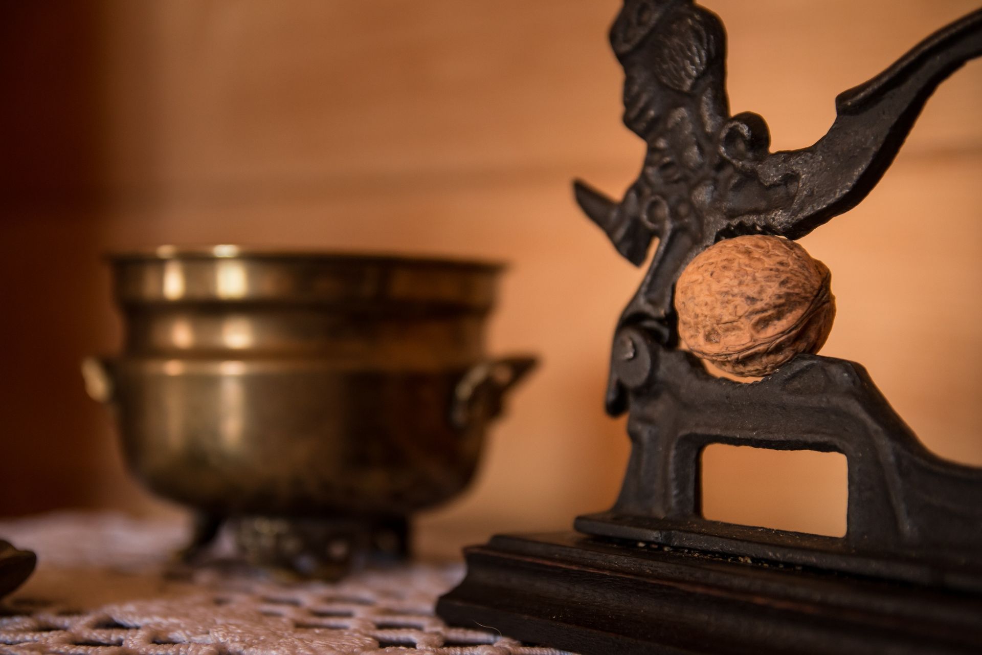 Close-up of a vintage nutcracker holding a walnut beside an antique brass bowl on a lace-covered table.