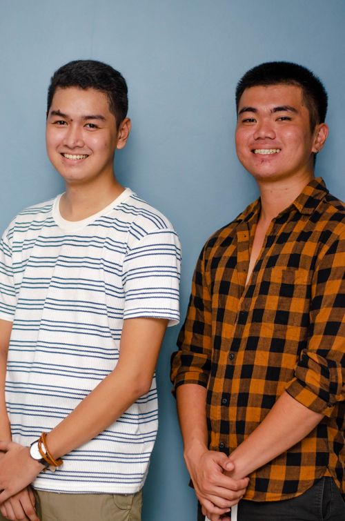 Free Two young men smiling and posing in a studio against a blue background, wearing casual shirts. Stock Photo