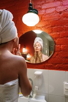 Woman performing daily skincare routine in modern bathroom with red wall and mirror reflection.