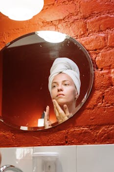 A woman applies skincare cream in a cozy bathroom setting, mirrored reflection.
