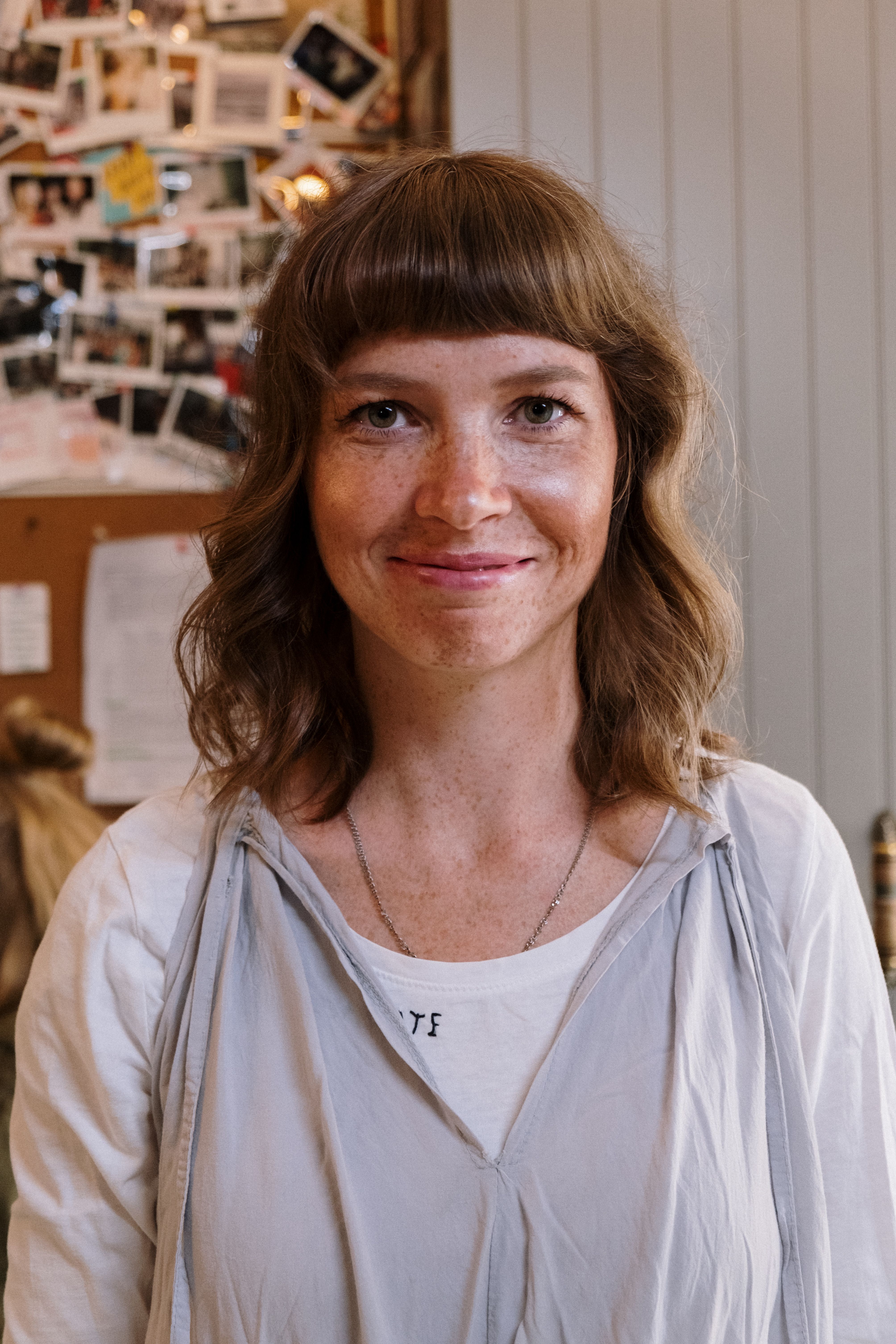Close-up portrait of a smiling woman indoors with a background of photographs.