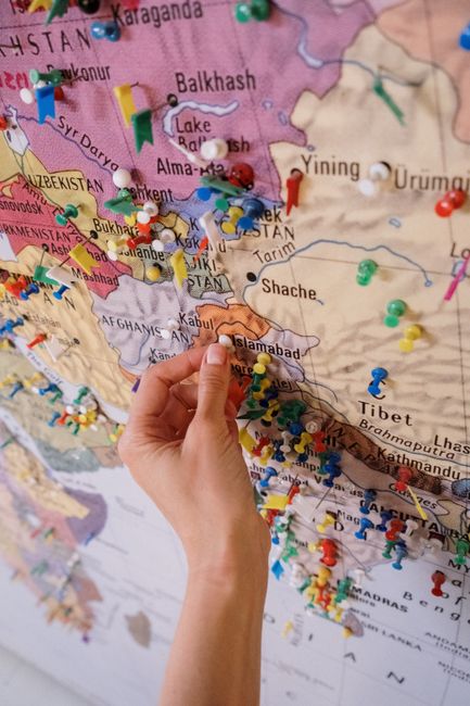A hand places pins on a colorful map highlighting locations in Asia.