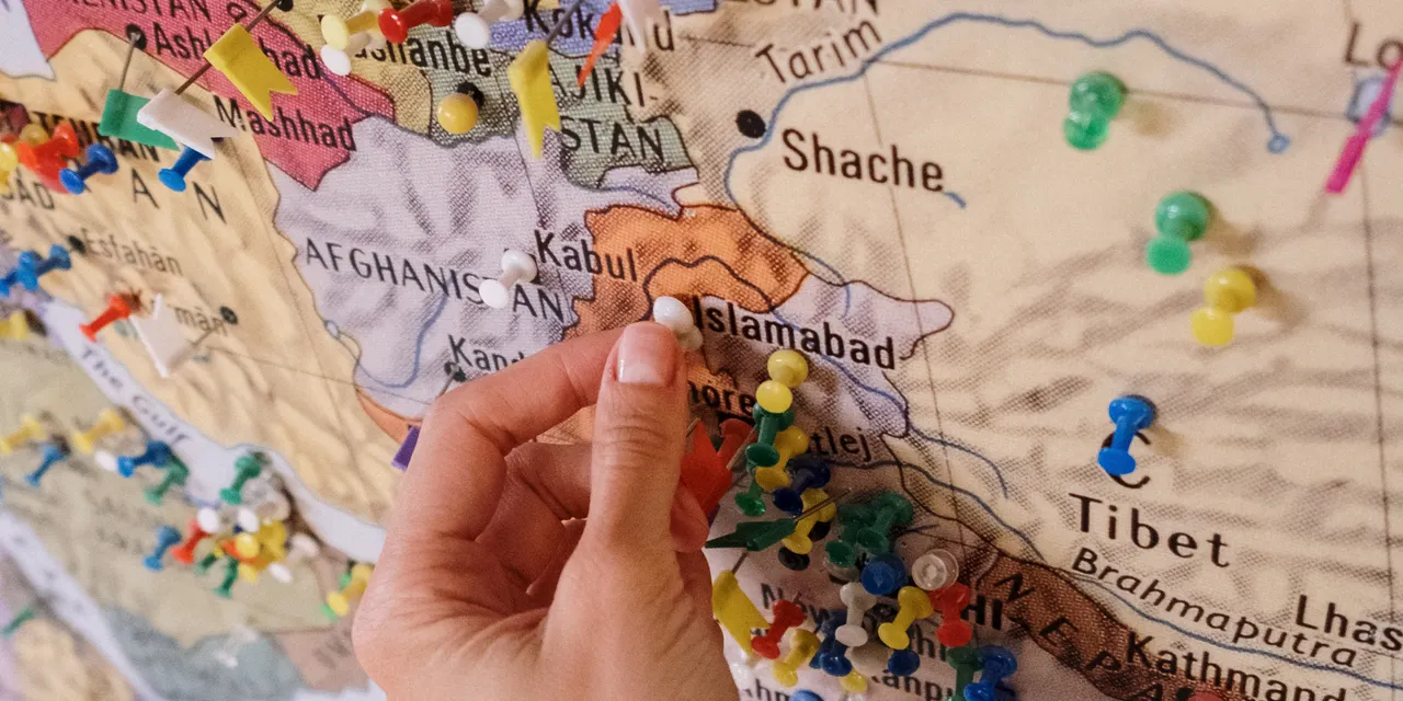 A hand placing coloured pins on a map to mark multiple business locations — the core challenge of multi-location SEO
