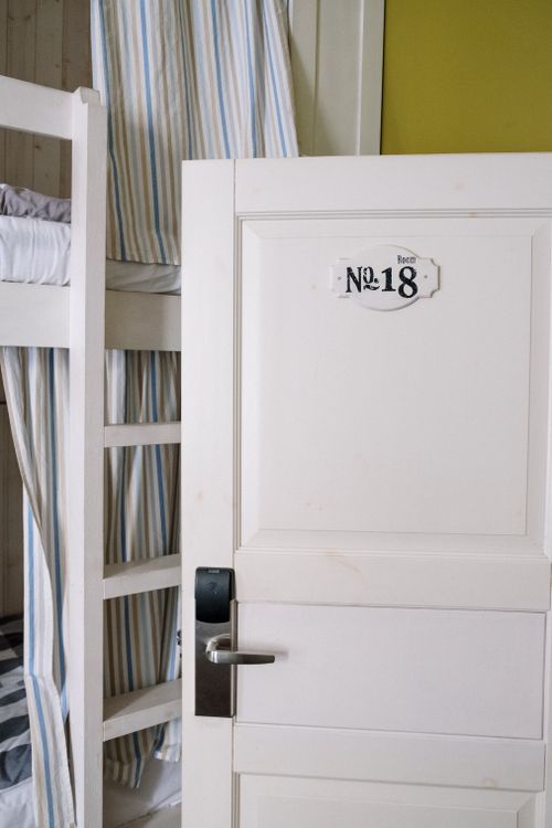 Free Cozy hostel room with a white door labeled No. 18 and bunk bed. Stock Photo