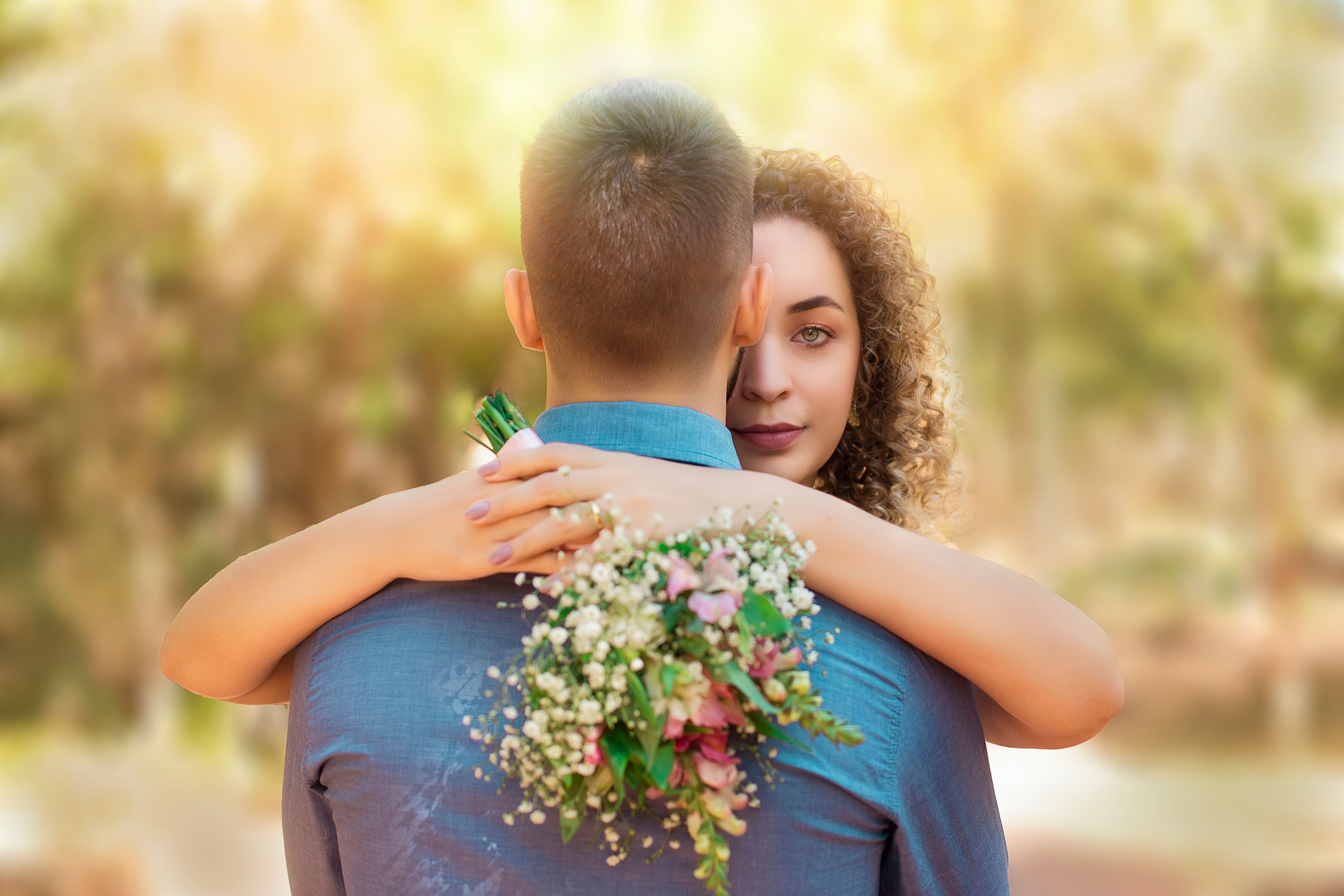 An intimate outdoor moment capturing a couple hugging with a floral bouquet.