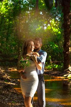 A joyful couple embracing by a forest stream, surrounded by nature's beauty.