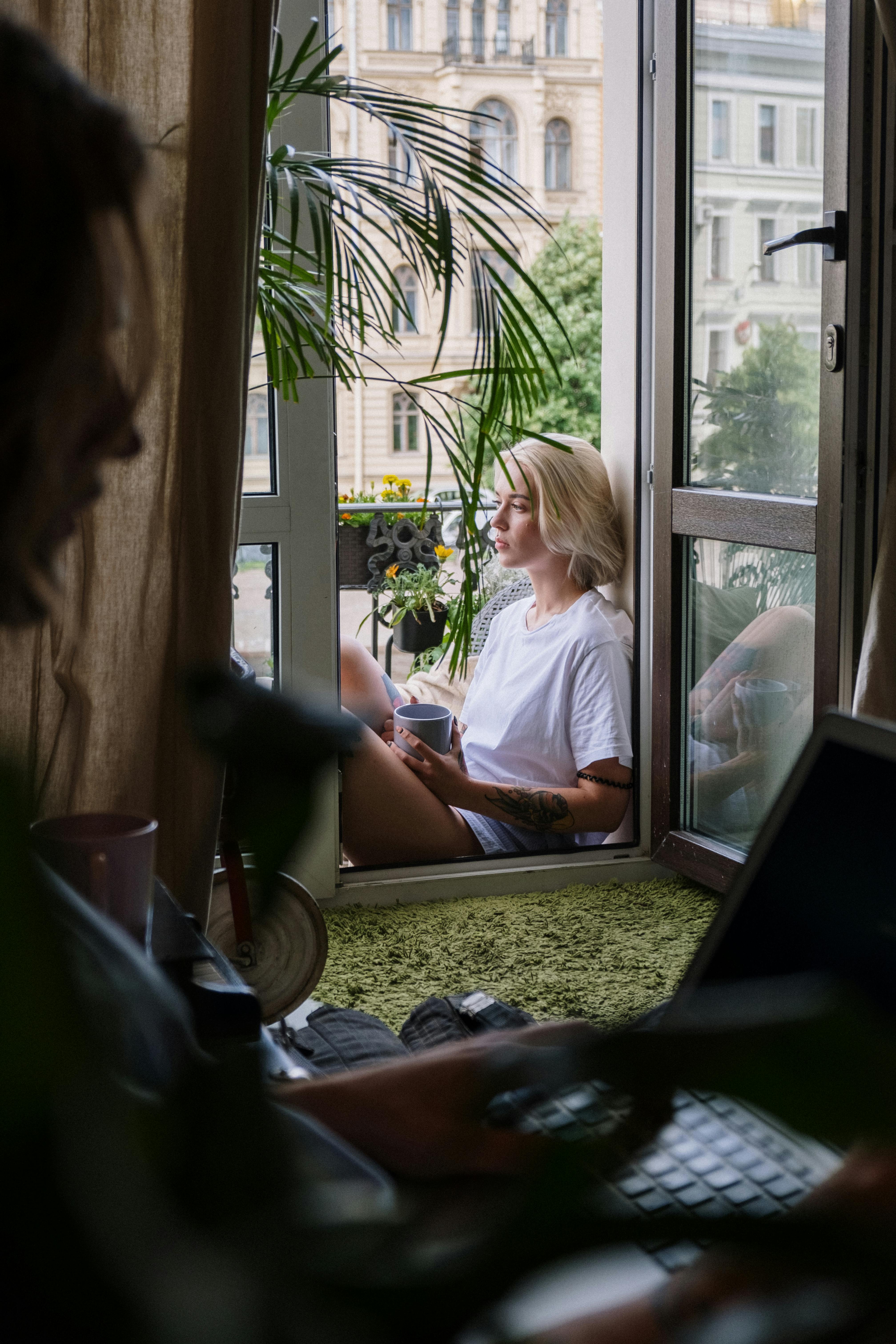 A blonde woman sits on a balcony, enjoying a peaceful moment with a cup of coffee.