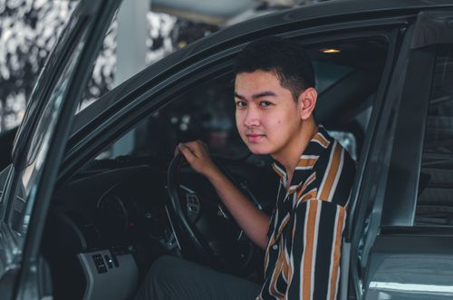 Free A young man smiling while sitting in a car, captured outdoors. Perfect for themes of travel and lifestyle. Stock Photo