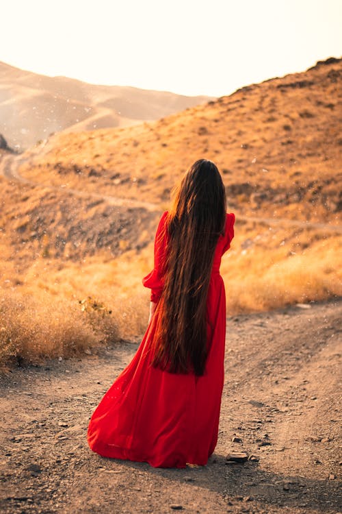 Woman in Red Dress Standing on Dirt Road