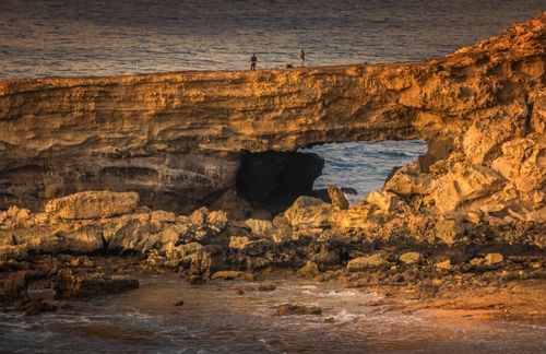 Free A stunning coastal view highlighting a natural rock arch at sunset with the ocean waves. Stock Photo