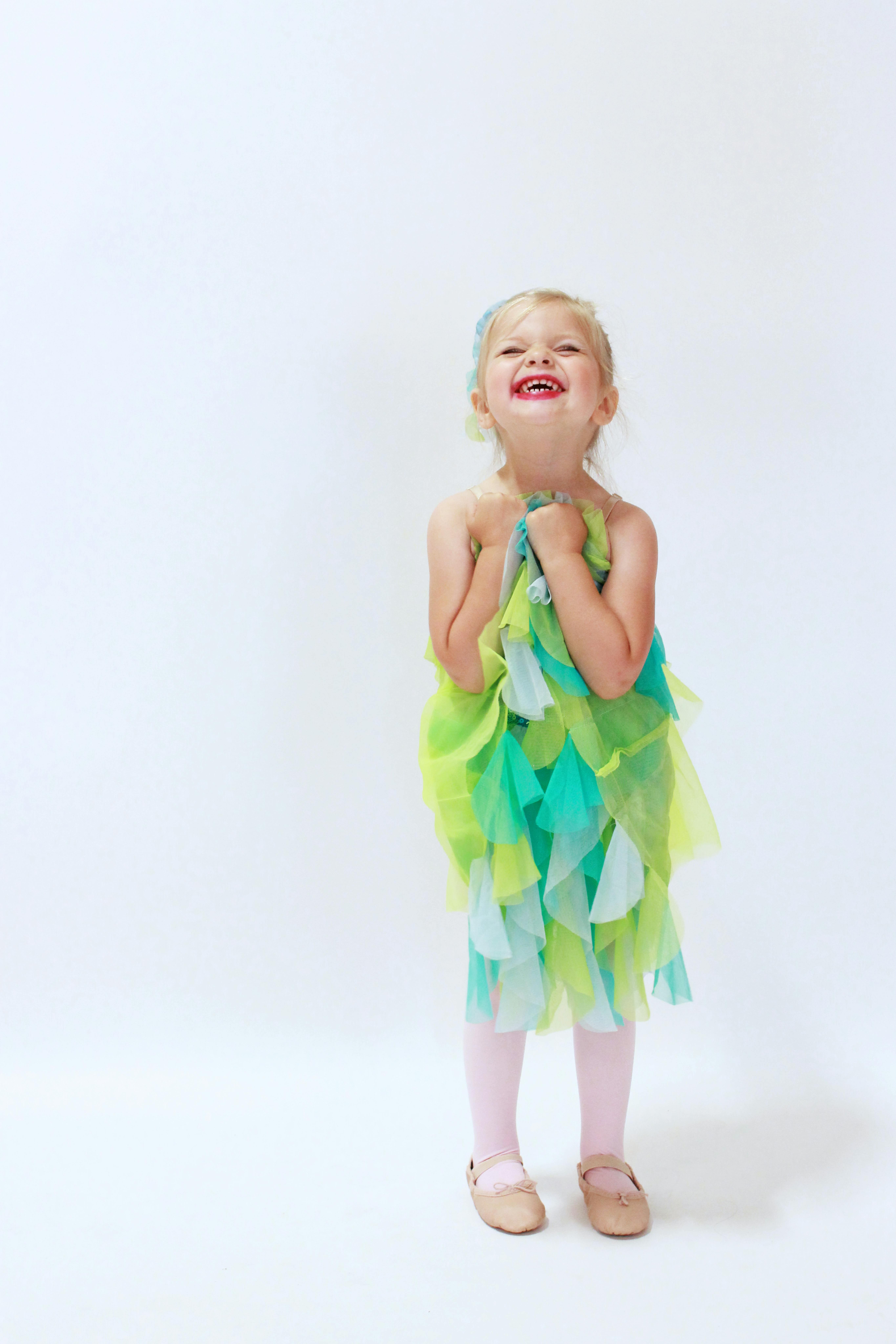 在明亮的工作室环境中，一个穿着彩色连衣裙的快乐年轻女孩开心地笑着