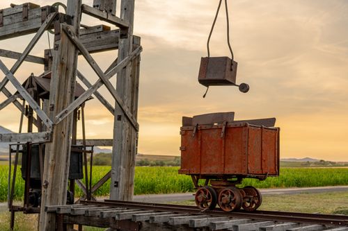 Free A vintage rusty mining cart on tracks with a wooden support structure during sunset. Stock Photo