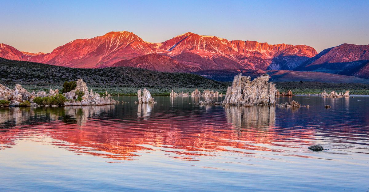 Stunning sunrise view of tufa formations reflecting in Mono Lake, California, with mountains in the background.