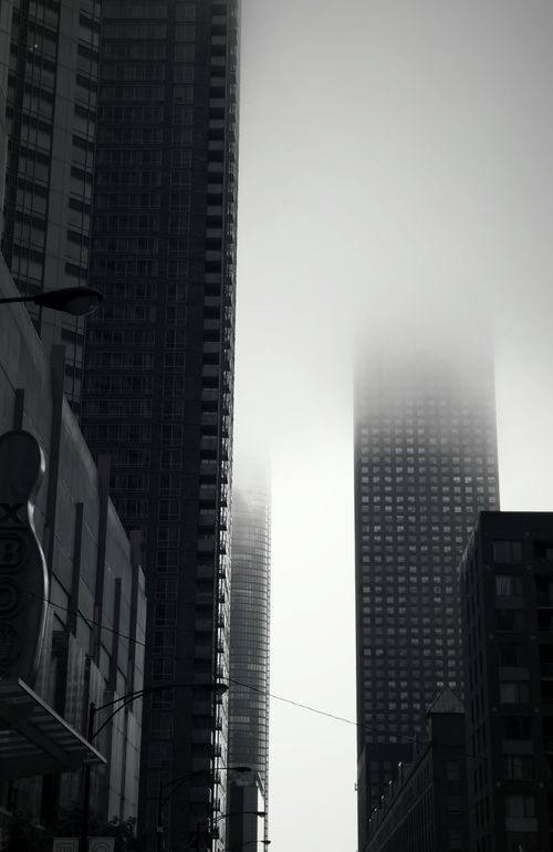 Free A vertical shot of tall skyscrapers shrouded in fog, creating a dramatic urban scene. Stock Photo