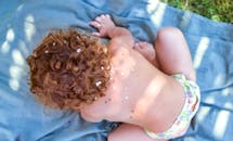 卷发幼儿在户外玩耍，毯子上撒着五彩纸屑