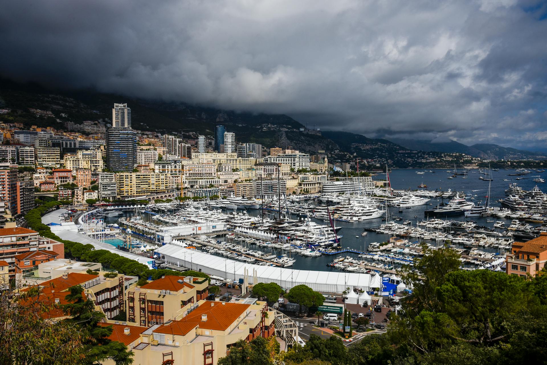 A stunning aerial view of Monaco City with luxury yachts docked at the harbor under an overcast sky.