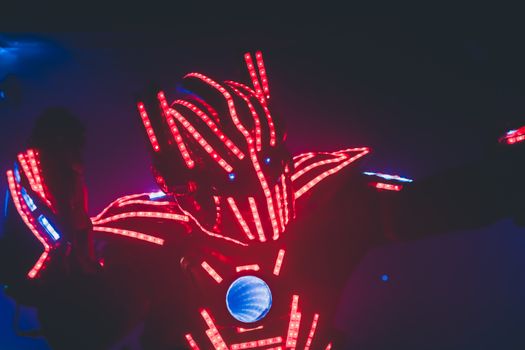 Unrecognizable man in costume with glowing light emitting diodes giving performance in twilight