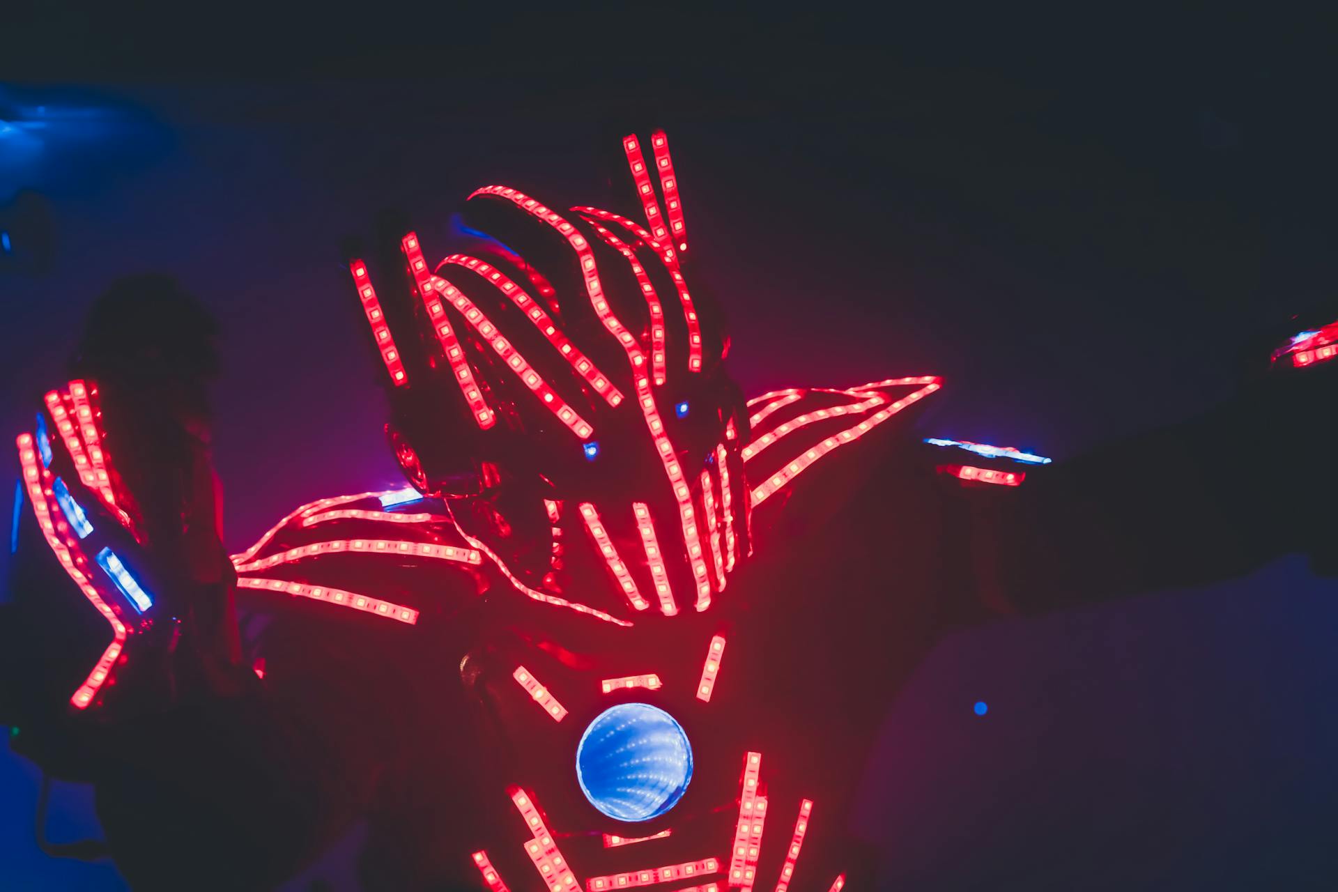 Unrecognizable man in costume with glowing light emitting diodes giving performance in twilight