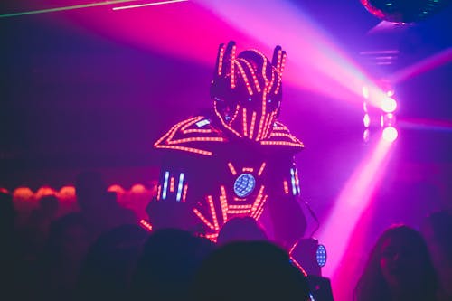 Anonymous person in illuminated futuristic costume of robot performing show on stage of modern nightclub with neon illumination
