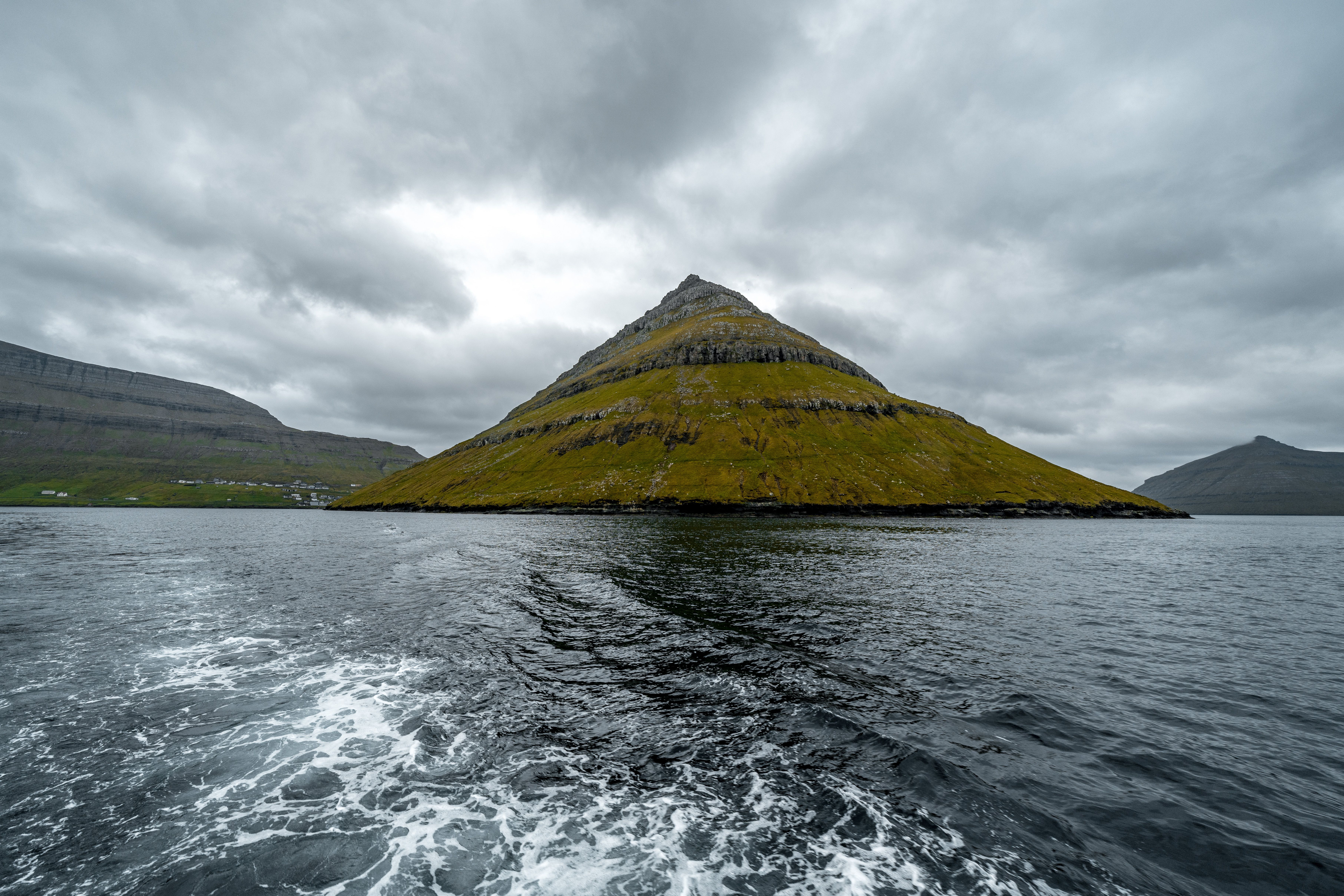 Scenic view of a unique pyramid-shaped mountain rising from the ocean under a cloudy sky in the Faroe Islands.