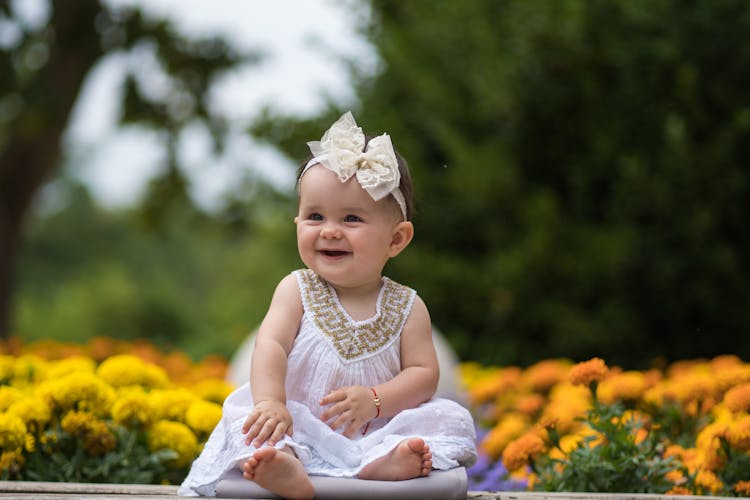 Smiling Little Baby Infant Sitting Outdoors Near Flowers