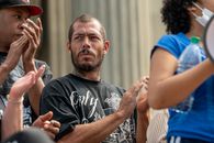 Serious bearded man in casual clothes standing on street with unrecognizable multiracial people and applauding during protests against racial discrimination