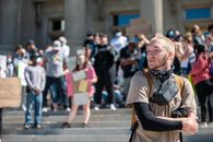Pensive young bearded guy in casual clothes and backpack standing on street with group of protesting people and looking away during BLM demonstration