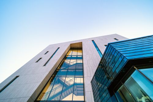 Free From below of modern geometric building with glass details and staircase inside against cloudless blue sky Stock Photo