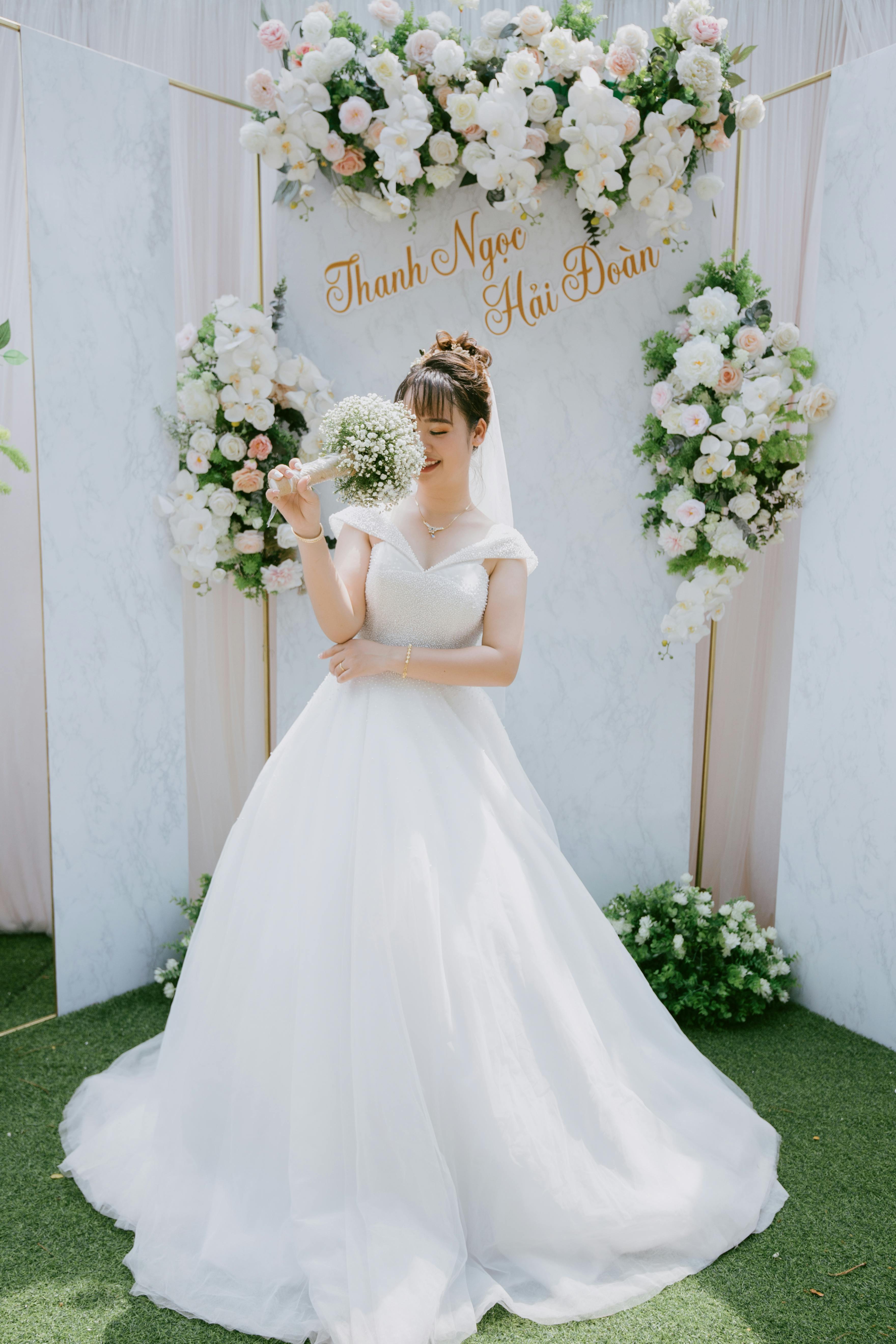 A beautiful bride in a classic white gown holds a bouquet, surrounded by elegant floral wedding decor.