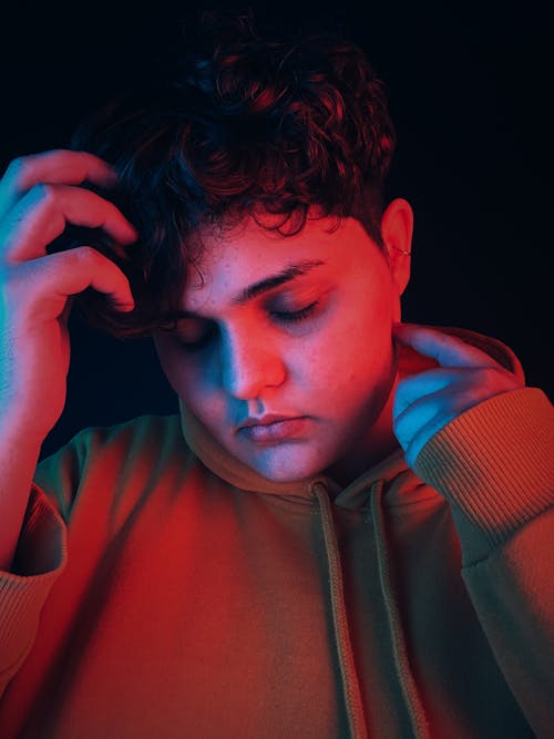 Calm male with eyes closed touching hair lightened by red light in dark room with black background