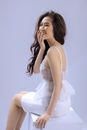 一位微笑的女子穿着白色连衣裙坐在室内，显得欢乐而优雅