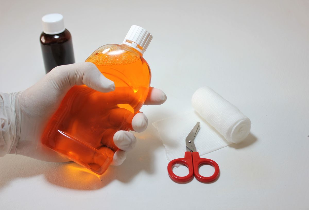 Hand holding antiseptic beside bandages, gauze, scissors, and first aid supplies
