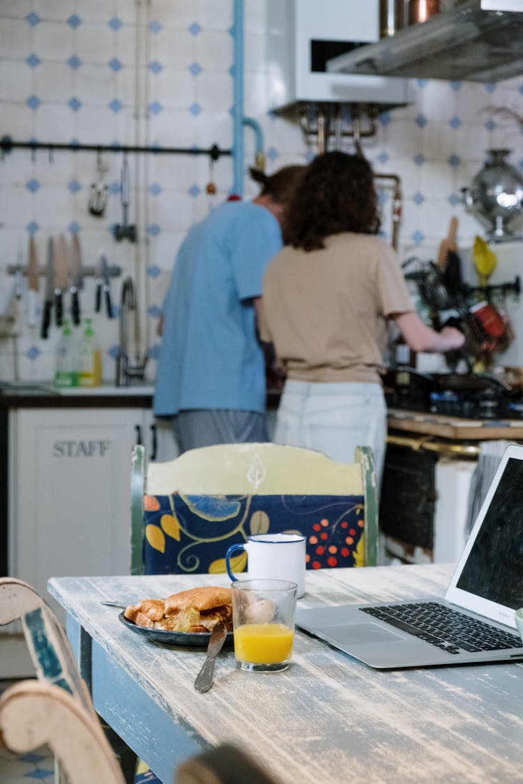 Woman And Man Standing Behind Table With Laptop And Food In Kitchen