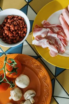 Vibrant overhead shot of bacon, tomatoes, beans, and mushrooms on colorful plates.