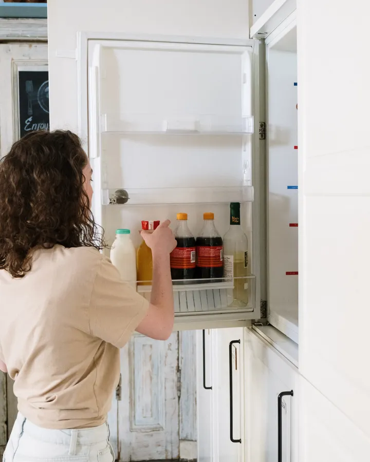 Frigidaire refrigerator repair in La Mesa, CA Woman reaching for a bottle in a kitchen refrigerator, Frigidaire refrigerator repair in La Mesa