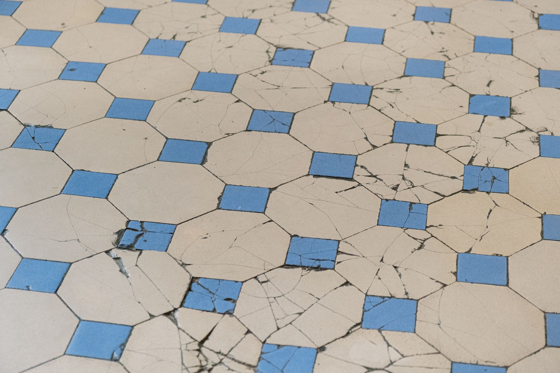 A detailed view of aged cracked tiles with a blue and white geometric pattern.