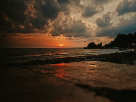 Capture of a dramatic sunset with dark clouds over a serene beach shrouded in twilight.