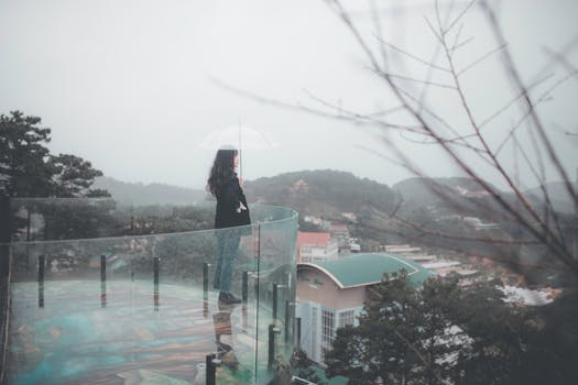 一名妇女撑着伞，站在玻璃阳台上俯瞰雾气缭绕的城市景观