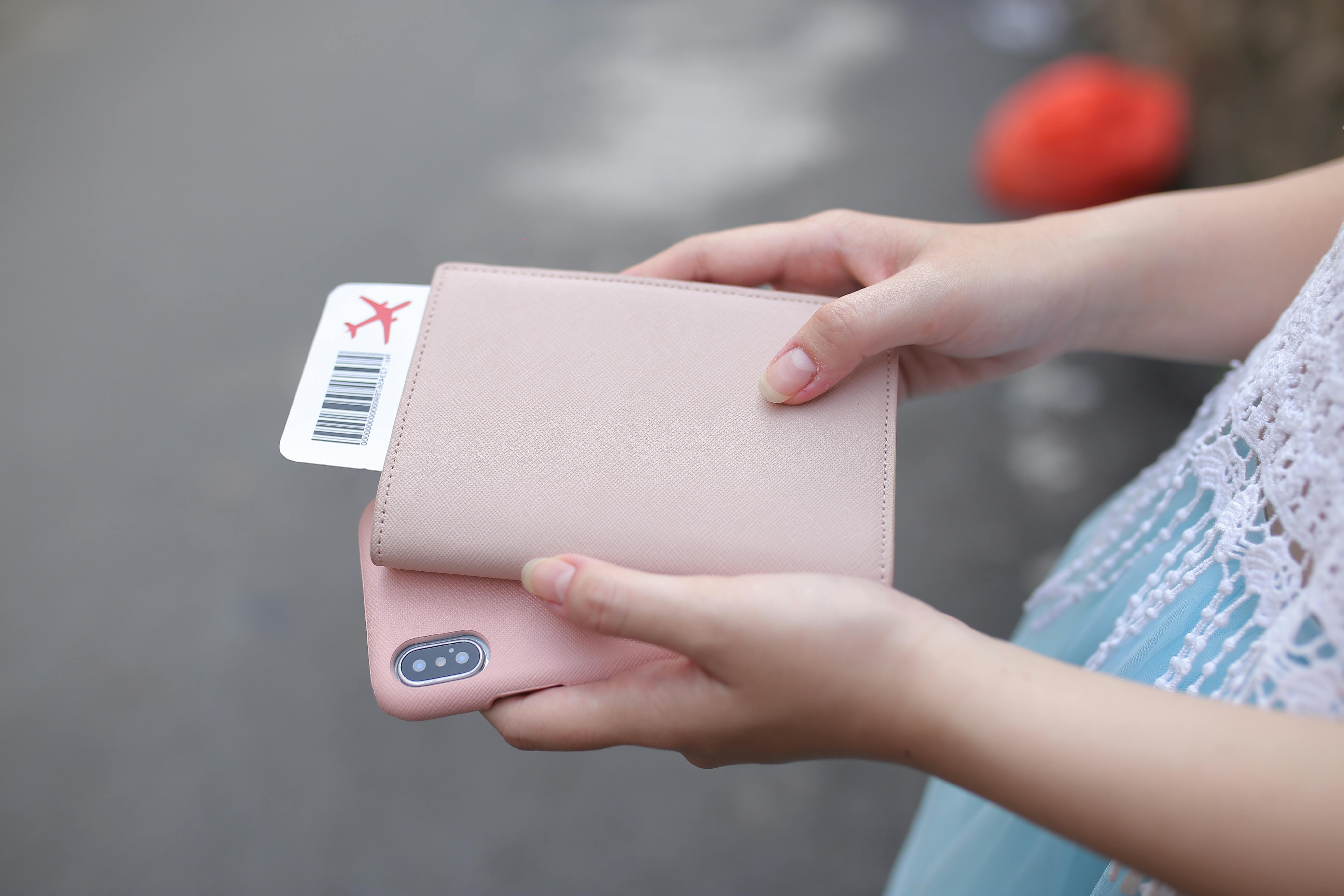 Person holds a passport wallet, phone, and boarding pass while preparing for air travel