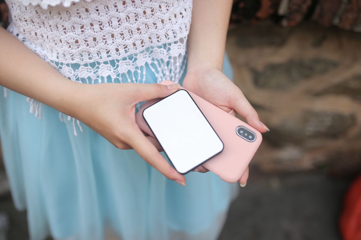 Handen houden een compacte witte powerbank en een smartphone met roze hoesje vast