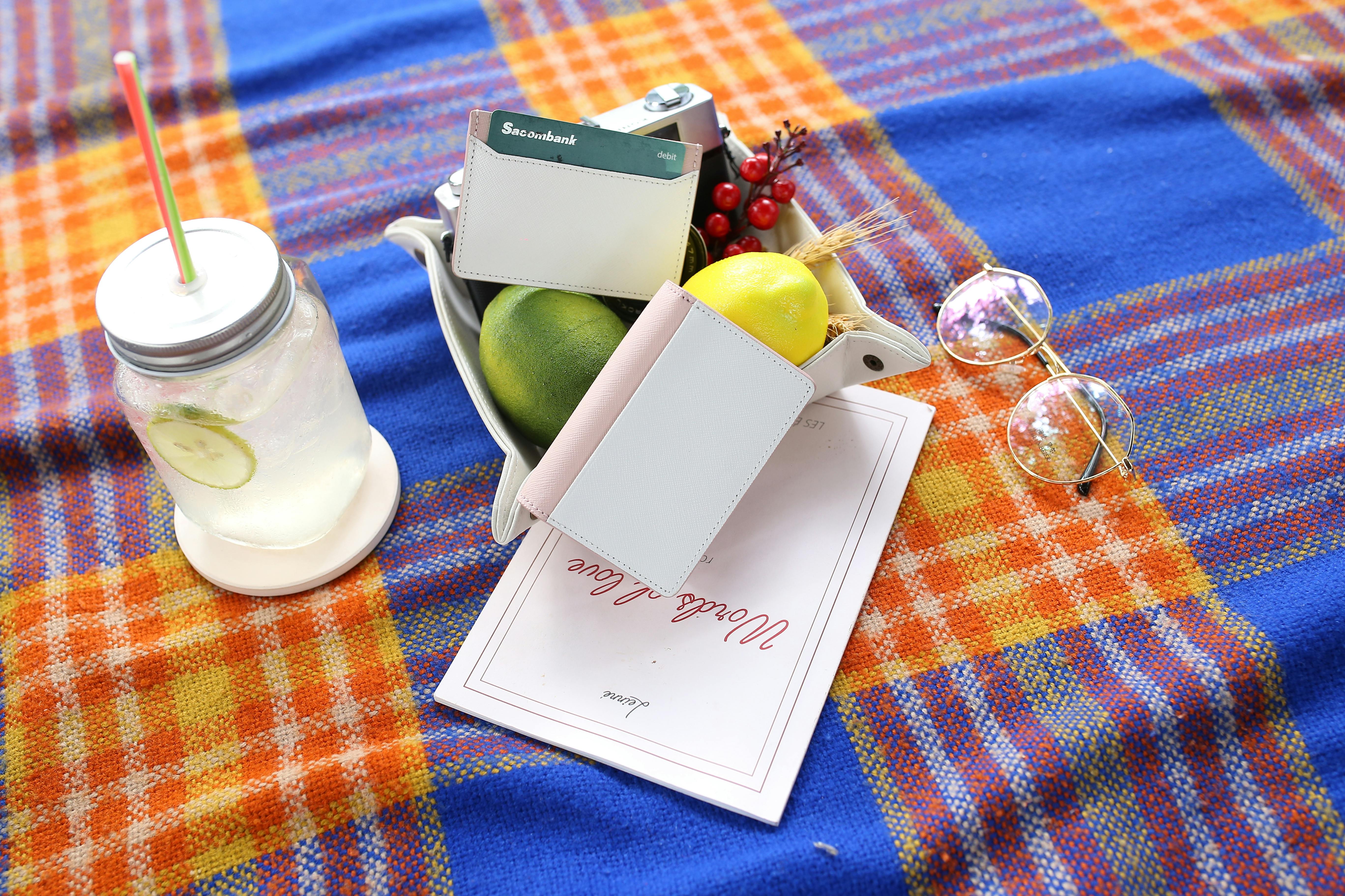 Top view of a colorful picnic setting with a cold drink, fruits, and accessories.