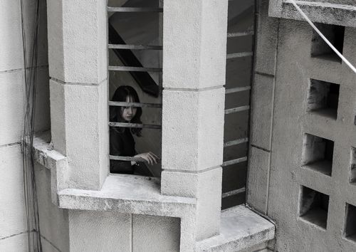 Free Woman standing behind concrete bars adds mystery to the architectural scene. Stock Photo