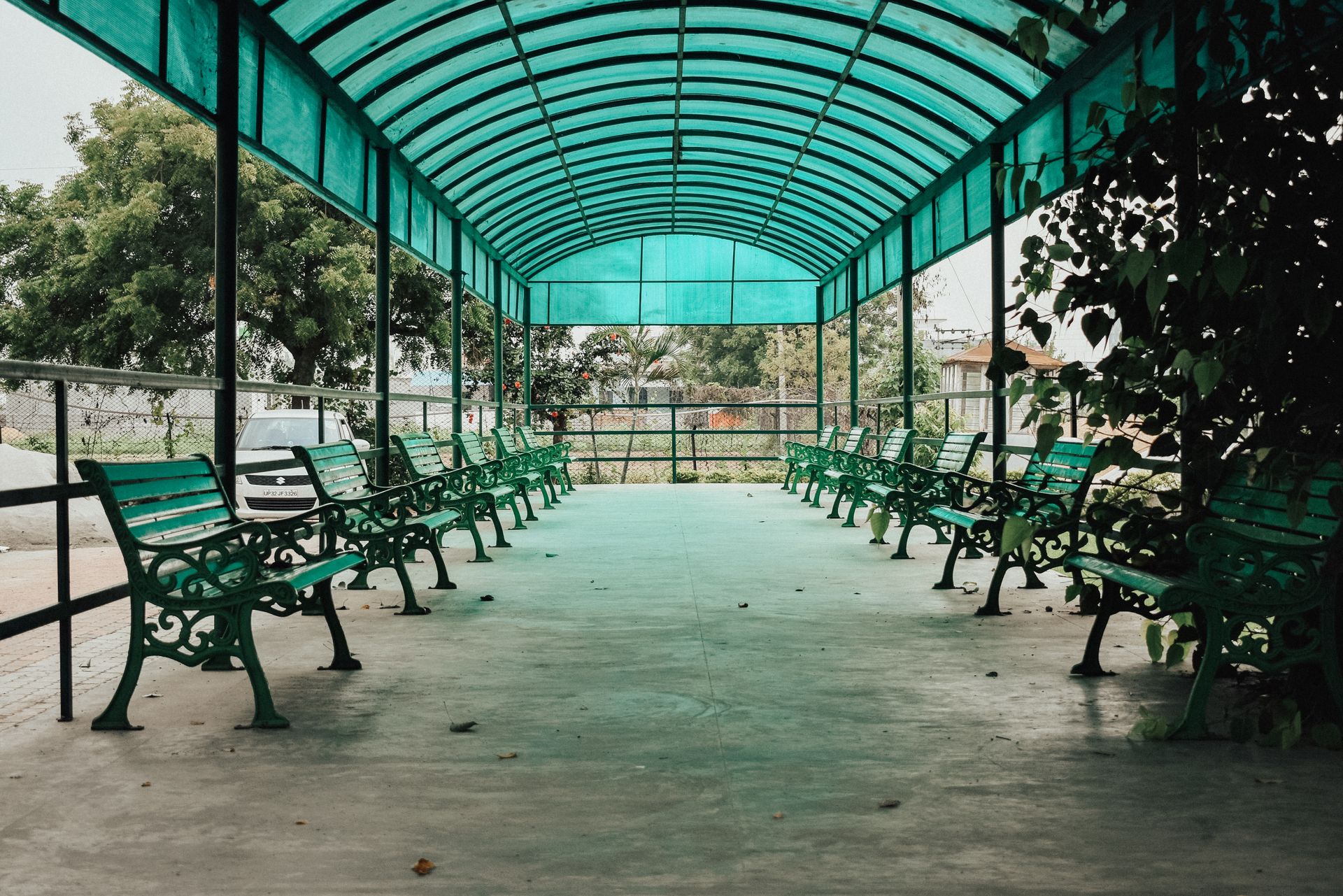 A quiet urban park walkway with green benches under a glass canopy, offering a peaceful retreat.