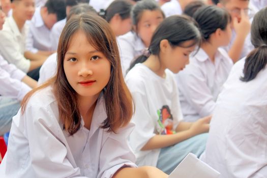 Asian teenagers in white uniforms gathered in an outdoor setting for study.