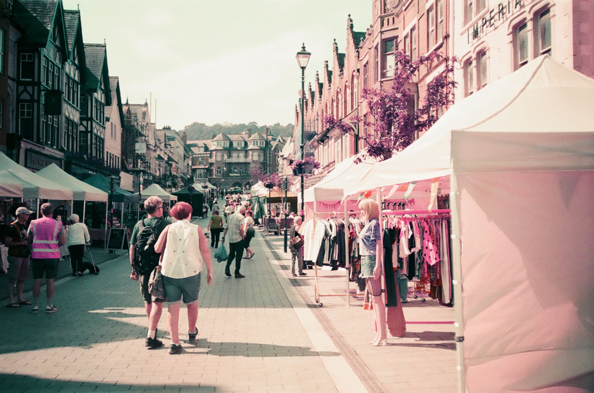 A vibrant street market with people shopping and colorful stalls on a sunny day.
