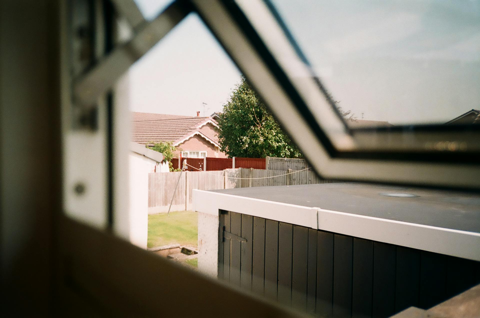 A serene view of a suburban backyard seen through an open window, capturing houses and greenery.