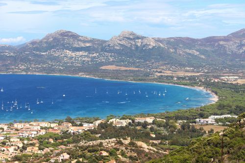 Free Drone view of boats floating on water surface near grassy shore with coastal settlement with mountainous area in distance against cloudy sky Stock Photo